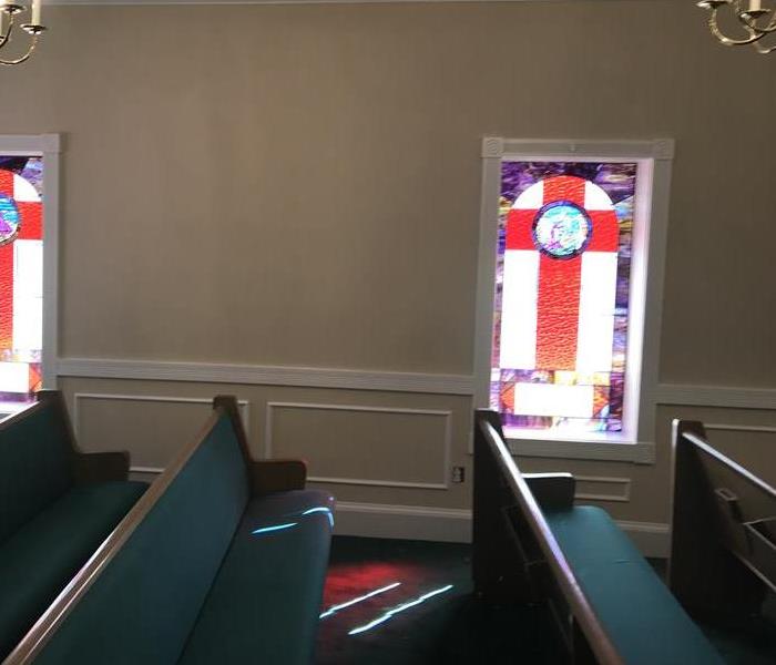 Wooden pews in church with white walls, carpeted and hardwood floors.