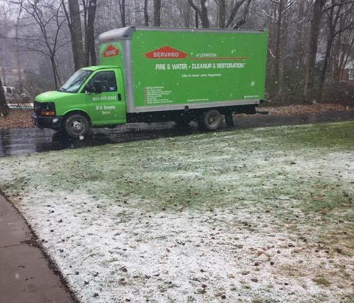 Green SERVPRO truck in a driveway with snow falling.