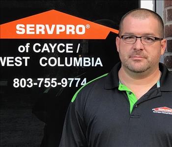 male with black polo on, standing in front of glass door with orange SERVPRO logo